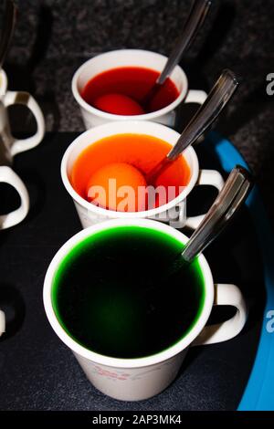 Coloring hard boiled Easter eggs in coffee cups, vertical Stock Photo