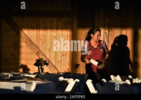 Middle ages Hispanic ethnic woman decorating table before a wedding reception in a barn for relatives with place cards with names Stock Photo