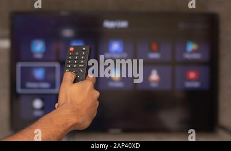 Maski, India 18,January 2020 - Hands holding remote control with different online subscription apps on TV screen in out of focus