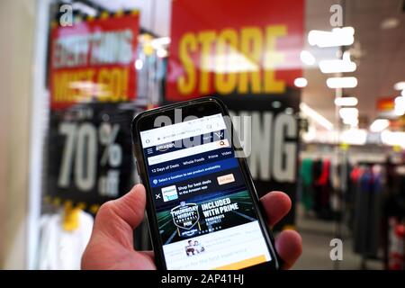 Storrs, CT USA. Dec 2019. Smartphone with online retailer Amazon homepage in hand of customer entering a store with permanently closing sign. Stock Photo