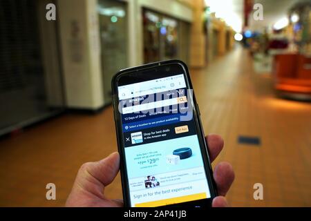 Storrs, CT USA. Dec 2019. Smartphone with giant online retailer Amazon homepage in hand of a visitor walking in an empty mall. Stock Photo