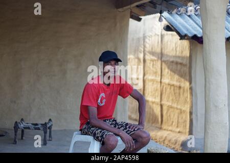 A man from Tharu cast sitting outside his traditional house in Bardiya Village Nepal Stock Photo