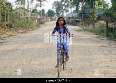 A young girl riding a bicycle on the dirt road of Bardiya Village in Nepal Stock Photo