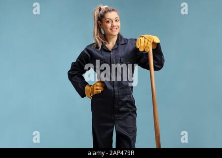 Female farmer in a uniform leaning on a working tool isolated over blue background Stock Photo