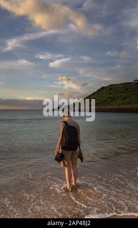 tourist with backpack standing in the sea at Hamdeok Beach at sunset Stock Photo