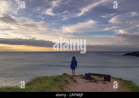 woman in blue dress standing at the edge of the hill near lava rock bench Stock Photo