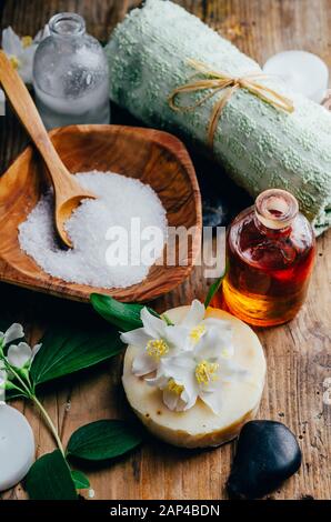 Natural spa cosmetics with essential massage oils, jasmine flower petals, zen stone on rustic wooden background. Handmade soap and herbal aromatherapy Stock Photo