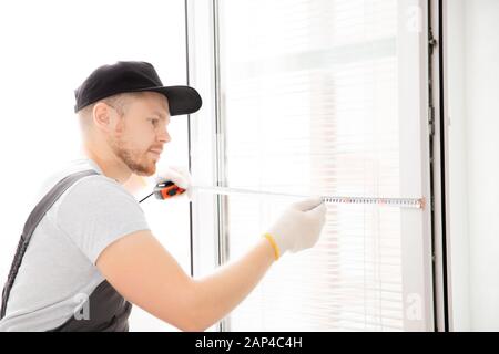 Worker in uniform installing blinds on plastic upvc window Stock Photo