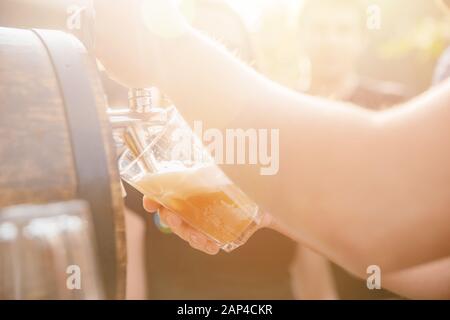 Craft beer is poured into glass mugs from wooden keg in summer, glare sun Stock Photo