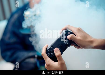 Man holds gamepad in hands, in background smoke from hookah Stock Photo