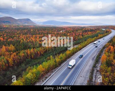 Forest autumn road with cars go sunset red, yellow trees russia, aerial view Stock Photo
