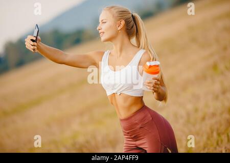 Beautiful blonde girl makes selfie photo on phone during sports training, smiling camera Stock Photo