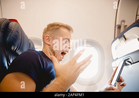 Man screams and resents cell phone on board airplane. Concept phobia and lack of internet addiction Stock Photo