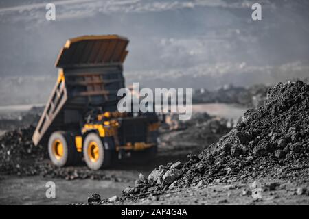 Close-up coal anthracite storage, in background large mining dump truck unloads ore Stock Photo