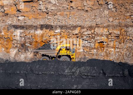 Big yellow mining truck laden anthracite moves open pit coal mine Stock Photo