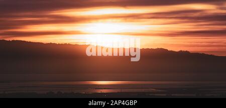 Sun setting behind the Santa Cruz mountains and reflected in the waters of San Francisco Bay; California Stock Photo
