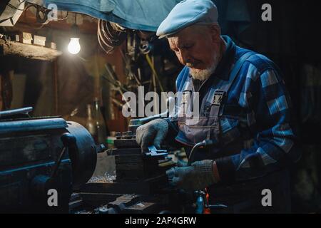 Senior elderly male turner handles metal on machine. Concept pension worker industrial, workplace Stock Photo