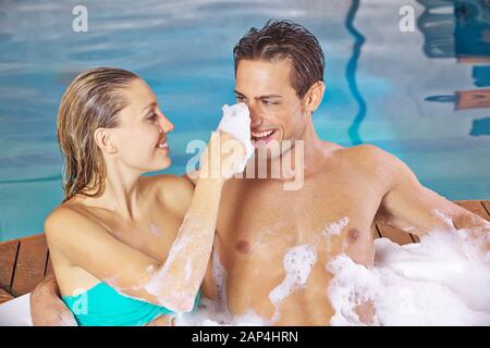 Happy couple is having fun in the jacuzzi with foam in the spa Stock Photo