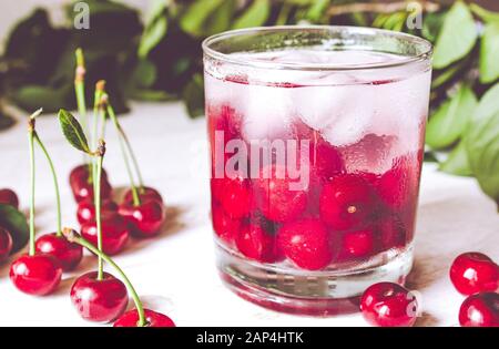 Fresh cherry cocktail with ice on a white wooden background. Fresh summer cocktail with cherries and ice cubes. Close-up. Stock Photo