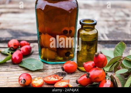 Bottle of rosehip seed essential oil near a jar with tincture and fresh red berries on a wooden table. Rosehip tincture or essential oil. Spa herbal m Stock Photo