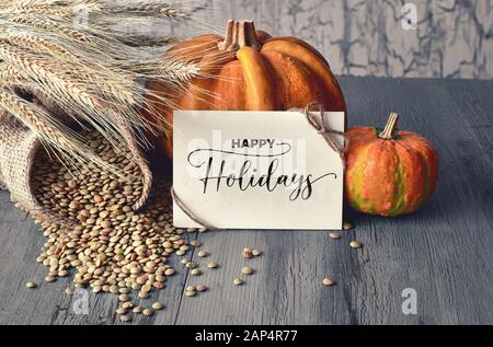 Autumn harvest still life with pumpkins, wheat ears and lentils in sack on faded blue rustic wooden background. Paper card with greeting 'Happy Thanks Stock Photo