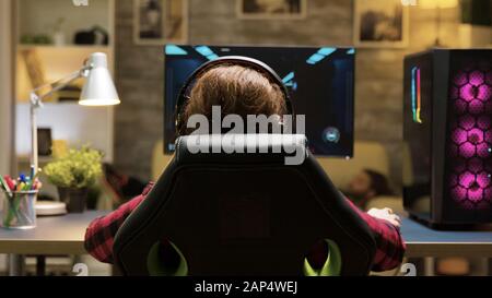 Dolly shot of woman sitting on gaming chair playing computer games. Man lying on sofa in the background. Stock Photo