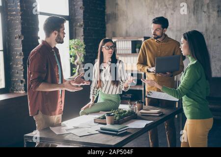 Company of four nice focused busy hardworking skilled qualified intelligent people professional IT specialists discussing profit growth at industrial Stock Photo