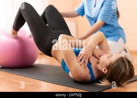 Physiotherapist working with young female client on core strength using fitball. Rehabilitation and physiotherapy background. Stock Photo
