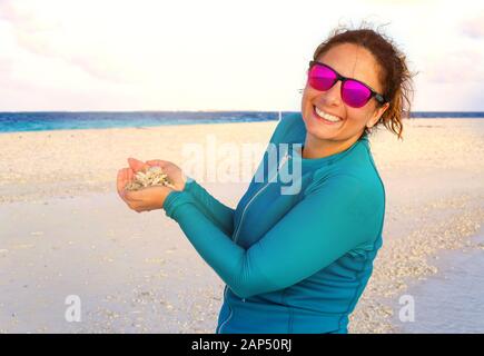 Young tourist takes a souvenir photo in the Maldives. In his hand shells and corals found on a strip of sand after low tide. Stock Photo