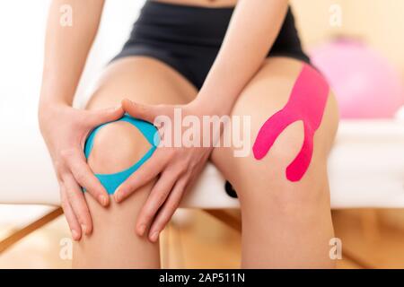 Young sportive female athlete holding her injured knee after treatment with kinesio tape. Close up. Kinesiology, physical therapy, rehabilitation conc Stock Photo