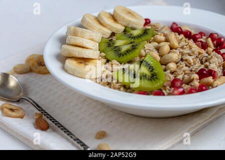 Breakfast consisting of oatmeal, nuts and fruits. Kiwi, banana, pomegranate and almonds decorate the plate. Healthy food, on a white background. Copy Stock Photo