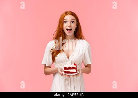 Surprised and amused charismatic redhead girl gossiping during party, holding plate with cake and open mouth fascinated as talking on birthday event Stock Photo