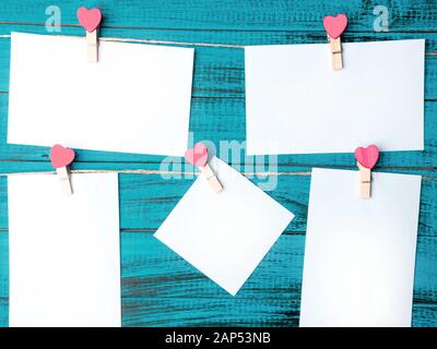 White stickers on trendy color blue wall design background. Valentine's Day concept. Symbol of love, copy space. Clothes pegs with red wooden hearts. Stock Photo