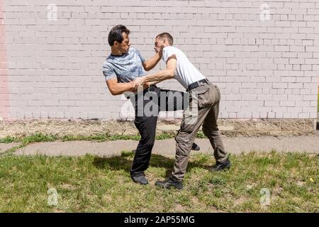 Mature male instructor strikes an attacker with a knee. Self Defense Techniques Krav Maga Stock Photo