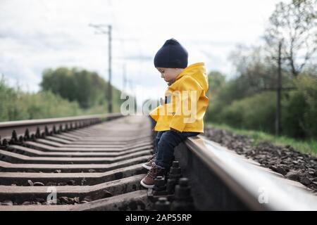 Kid in yellow jacket sitting on railroad Stock Photo
