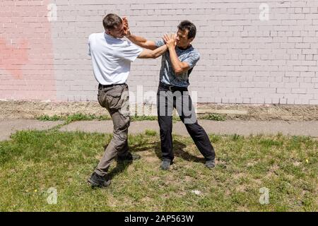 A mature male instructor strikes the attacker with a palm in his face. Self Defense Techniques Krav Maga Stock Photo