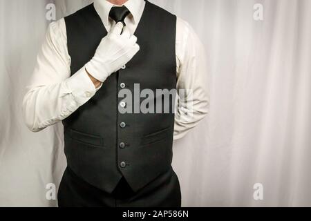 Man in Waistcoat and White Gloves Straightening Tie. Concept of Service Industry and Professional Hospitality and Courtesy. Stock Photo