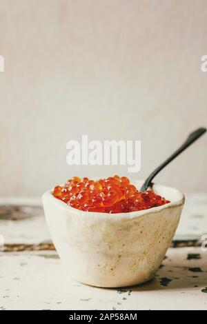 Red salmon caviar in ceramic bowl with spoon on old wooden table. Rustic style, copy space Stock Photo