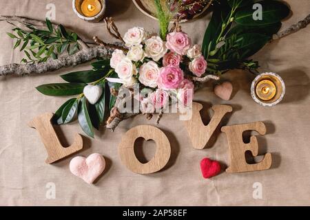 St. Valentines day or wedding romantic table setting with wooden letters love, needle felted hearts, bouquet of pink roses and red grapes on natural l Stock Photo