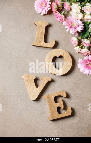 Word LOVE from oak wooden letters with variety of pink roses flowers over brown texture background. Flat lay, space. St. Valentines greeting card Stock Photo