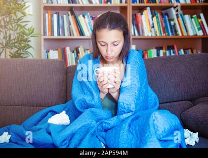Sick woman covered by a blanket on the sofa with high fever and flu