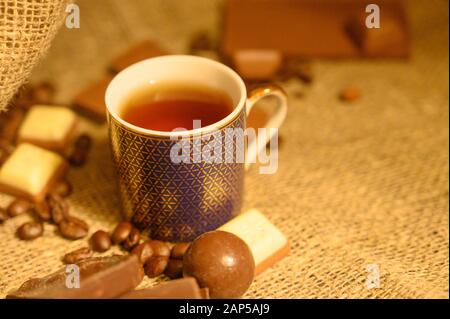 A mug of tea, chocolate and coffee beans on a background of rough homespun fabric. Close up Stock Photo