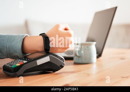 Woman working on laptop, using terminal for contactless payment via smartwatch for her order in cafe. New technology of NFC payment Stock Photo