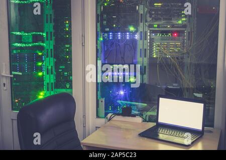 Empty workplace of the system administrator is in the server room. Many racks with computer equipment are behind the glass wall of a modern data cente Stock Photo