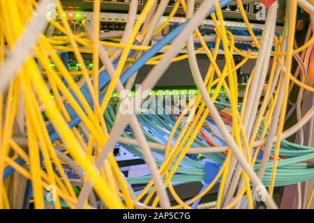 Chaotic intertwining of many Internet wires in the rack server room. Messy Communication cables are in the datacenter. Patch panel cabinet with comput Stock Photo