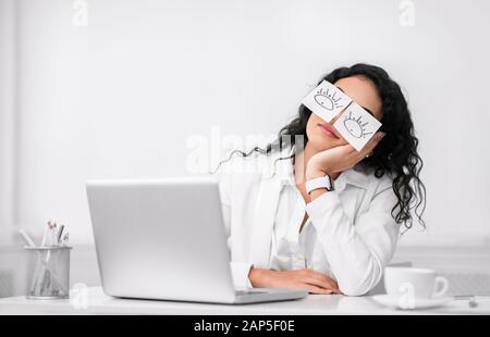 Young business man with fake eyes painted on paper stickers sleeping at  workplace in office Stock Photo