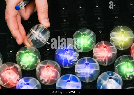 A man's hand inserts a round lamp into an electrical network. Colored light bulbs. LED lamp Stock Photo