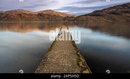 A long exposure of an old jetty on the shore of Loch Lomond, Scotland.  Looking over to Inversnaid and the mountains of Loch Lomond National Park. Stock Photo