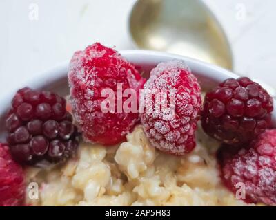 Breakfast consisting of oatmeal, nuts and fruits. Kiwi raspberries blackberries pomegranates almonds mint decorate a plate. Healthy eating, on a light Stock Photo