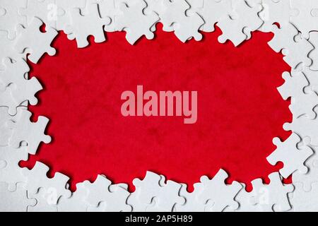 Framing in the form of a rectangle, made of a white jigsaw puzzle. Frame text and jigsaw puzzles. Frame made of jigsaw puzzle pieces on red background Stock Photo